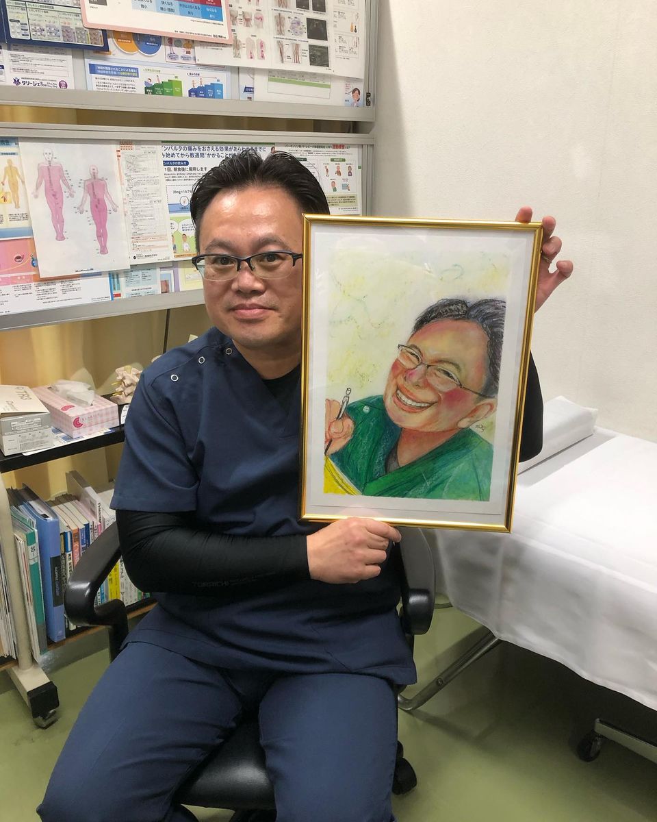 黄色い額に入った似顔絵を持つ、恵川 宏敏 先生