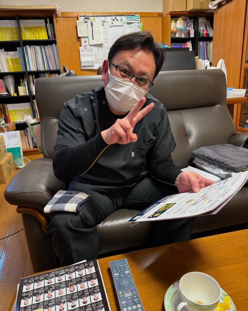 ソファに座って、ピースサインをする恵川先生