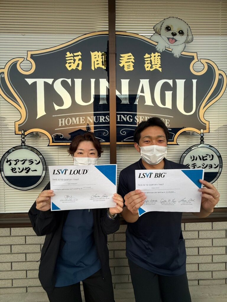 TSUNAGUの看板の前で、2名のスタッフがLSVT LOUDとLSVT BIGの認定証をそれぞれ手に持っている写真