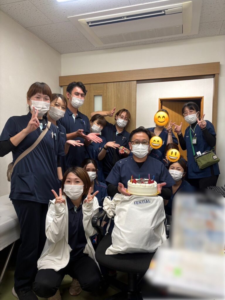 ケーキを持つ恵川先生と、その周りに集まったスタッフの集合写真（一部にぼかしと絵文字の加工あり）